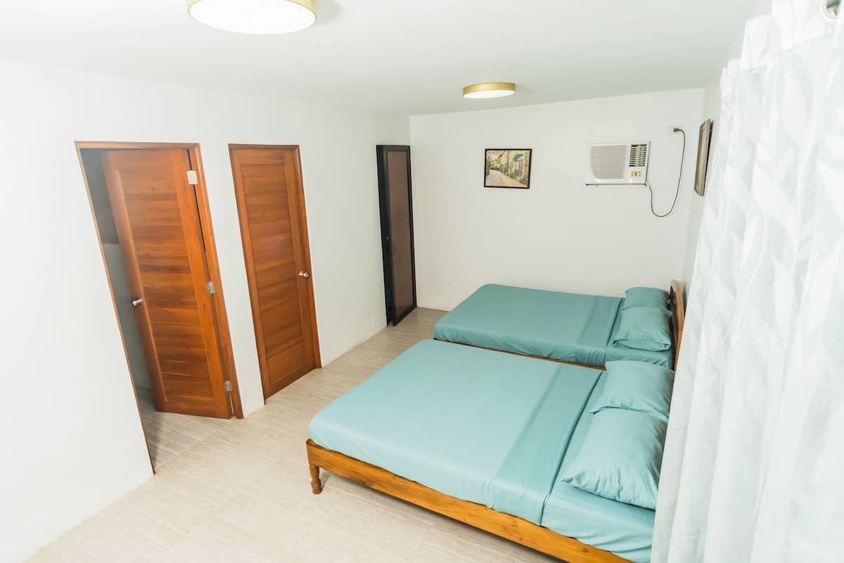 Ein Schlafzimmer mit zwei Betten, Holztüren, einem Deckenventilator und einem gerahmten Bild an der Wand.