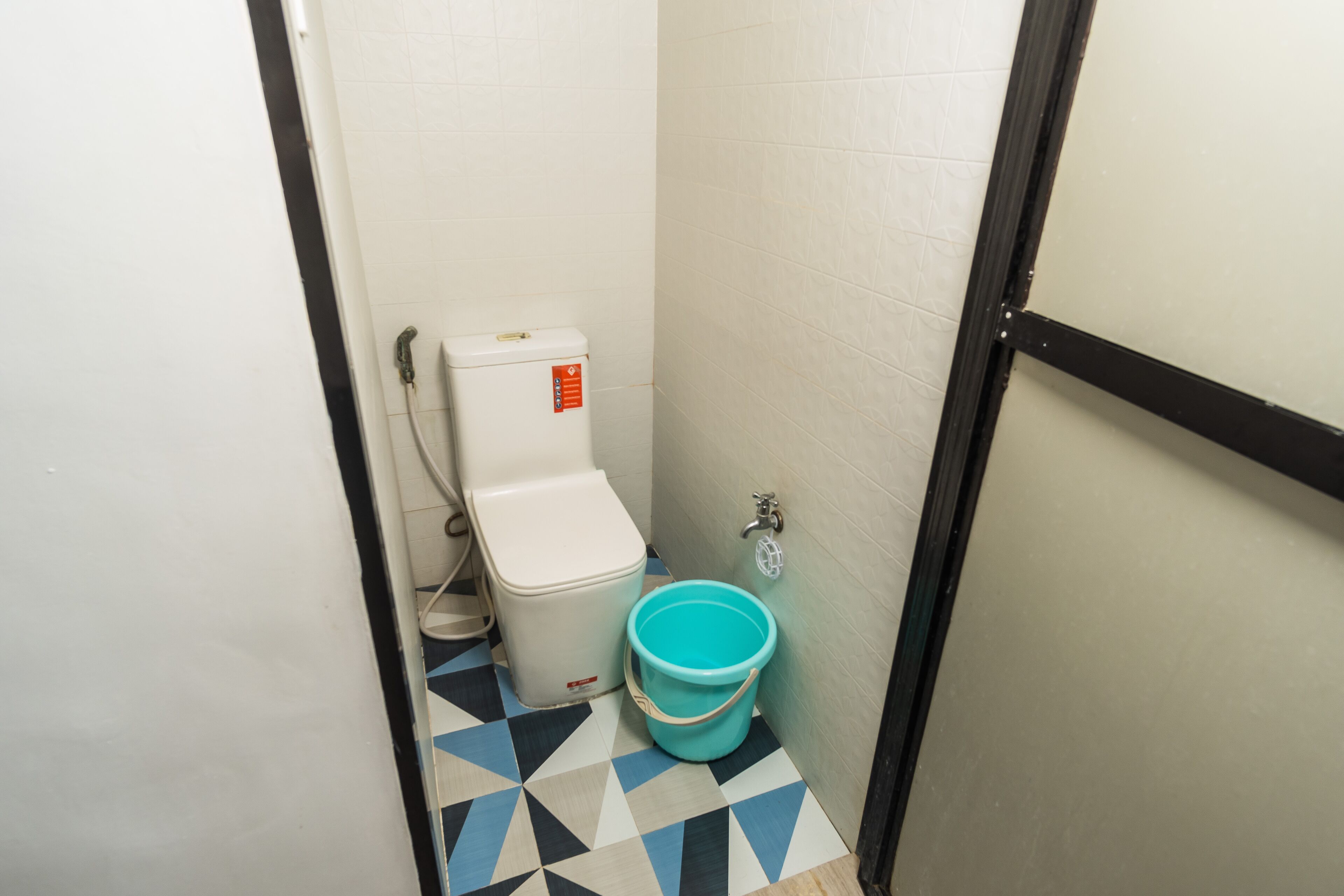 Une petite salle de bain avec des toilettes, un seau et un sol carrelé.