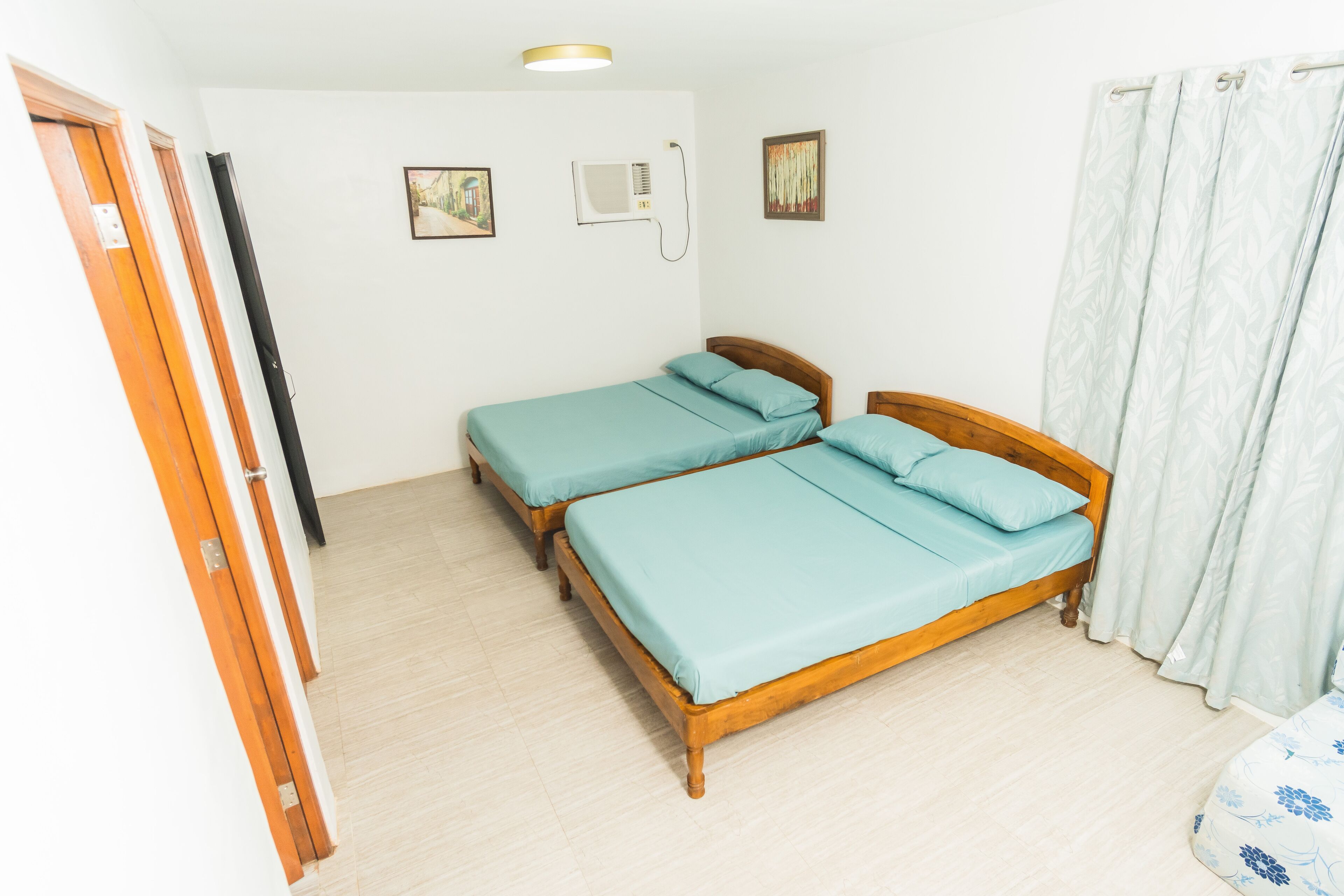 Ein Zimmer mit zwei Holzbetten, einem Deckenventilator und einem Fenster mit Vorhängen.