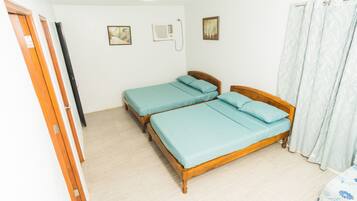 Una habitación con dos camas de madera, un ventilador de techo y una ventana con cortinas.