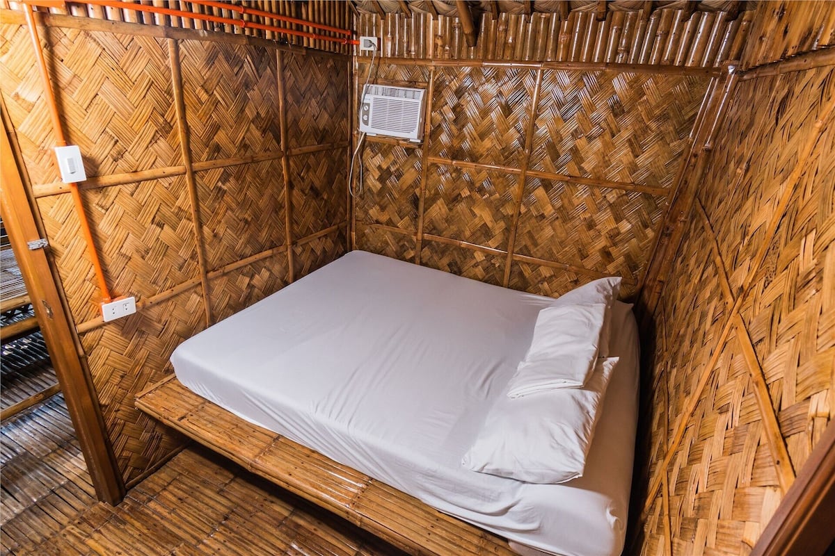 Ein Einzelbett in einem Zimmer mit Bambuswand und -decke, einer Steckdose und einem Thermostat an der Wand.