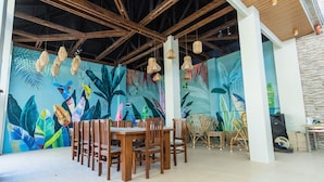 A dining area with wooden tables and chairs, a mural with tropical leaves, and hanging wicker lamps. - Villa Elizabeth Beach Resort (Lucena)