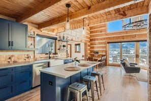 Una cocina amplia con una isla grande, techo de madera y vistas a montañas nevadas a través de ventanas amplias.