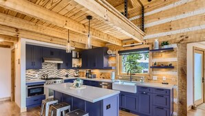 A modern kitchen with a large island, dark blue cabinets, and a wooden ceiling. - Lake Front! Mtn/Lake Views,HotTub,Gas FirePit,Walking Trail to town & shopping (Estes Park)