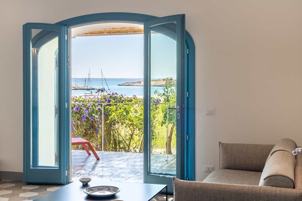 A room with a view of the sea, a table with a bowl, and a sofa.