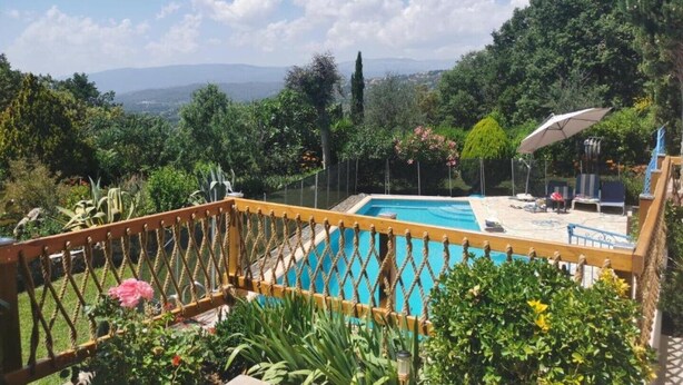 Zona de piscina con vistas a montañas, rodeada de abundante vegetación y una cerca de madera.
