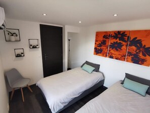 Ein modernes Hotelzimmer mit zwei Betten, einem Sessel, einer Tür und einer Wand mit einem floralen Gemälde.