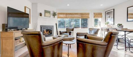 A living room with a fireplace, leather armchairs, a TV, and a dining area.