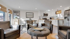 A modern living room with leather sofas, a round ottoman, and a kitchen in the background.