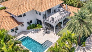 Ein zweistöckiges Haus mit Swimmingpool, Sitzgelegenheiten im Freien und einer überdachten Terrasse.