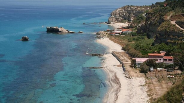 A coastal area with a beach, rocky outcrops, and buildings with red roofs. - Panoramic Santa Domenica (Santa Domenica)