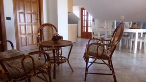 A dining area with wicker chairs and a round table, a wooden door, and a white table with striped chairs in the background. - Panoramic Santa Domenica (Santa Domenica)