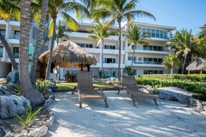 A resort with a pool area, lounge chairs, palm trees, and a building with multiple balconies.