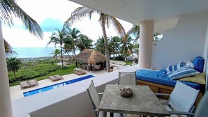 A balcony with a pool, lounge chairs, a table, and a bed with pillows.