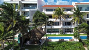 A modern hotel with a pool, palm trees, and a clear blue sky.