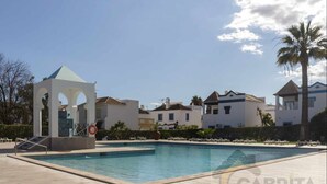 A swimming pool with lounge chairs, a gazebo, and villas in the background. - Casa Andorinhas - Quinta Velha Village - Free WiFi and Meo (Cabanas de Tavira)