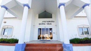 A building with a white facade, a central entrance with glass doors, and blue columns. - Casa Andorinhas - Quinta Velha Village - Free WiFi and Meo (Cabanas de Tavira)