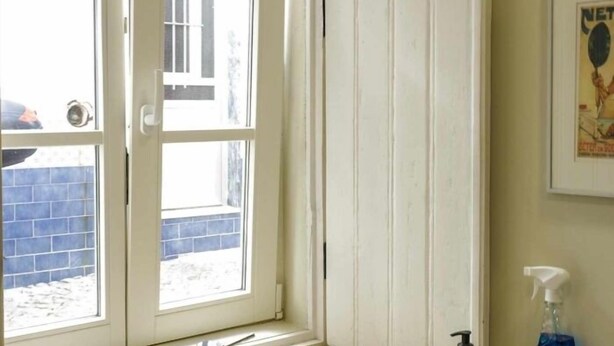 Ein Zimmer mit großem Fenster, einer Tür und einem an der Wand befestigten Poster.