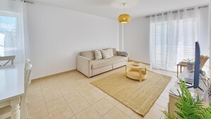 A modern living room with a beige sofa, a round coffee table, and a large window with sheer curtains.