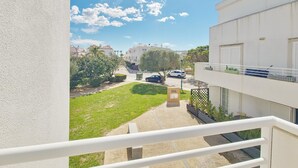 A residential building with a balcony, a paved courtyard, and a view of neighboring houses and cars.
