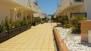 A corridor with tiled flooring, bordered by low walls with plants and a pebble garden.