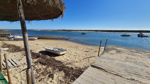 A beach with a wooden deck, a thatched umbrella, and several boats in the water.