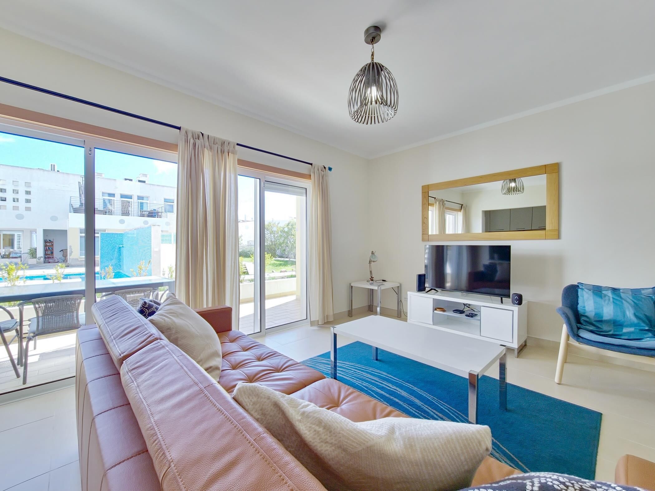 A modern living room with a sofa, TV, and a balcony with a pool view.