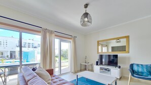 Ein modernes Wohnzimmer mit Sofa, Fernseher und einem Balkon mit Blick auf einen Pool.