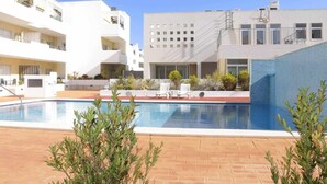 Ein Pool mit Liegestühlen und einer Pflasterterrasse, umgeben von modernen Gebäuden mit Balkonen und Fenstern.