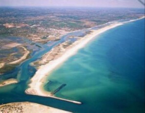 An aerial view of a coastal area with a long stretch of beach, a small peninsula, and a body of water.