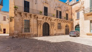 Un bâtiment historique aux détails architecturaux raffinés, une cour pavée et une voiture garée.
