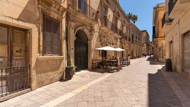 Une rue étroite bordée de bâtiments historiques, avec des terrasses et un café.