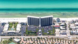 Vista aerea di un hotel costiero con un edificio centrale, parcheggi e una spiaggia sullo sfondo.