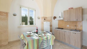 A compact kitchen with a dining area, featuring a window, a built-in stove, and a tiled backsplash. - 1756 Casina Farnarari - Appartamento 2 by Barbarhouse (Monteroni di Lecce)