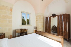 A bedroom with a bed, a desk, a chair, a window, and a wooden wardrobe with a mirror.