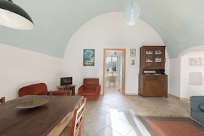 A spacious living room with a wooden dining table, two red armchairs, a television, and a cabinet.