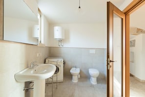A bathroom with a sink, washing machine, bidet, toilet, and wooden-framed door.