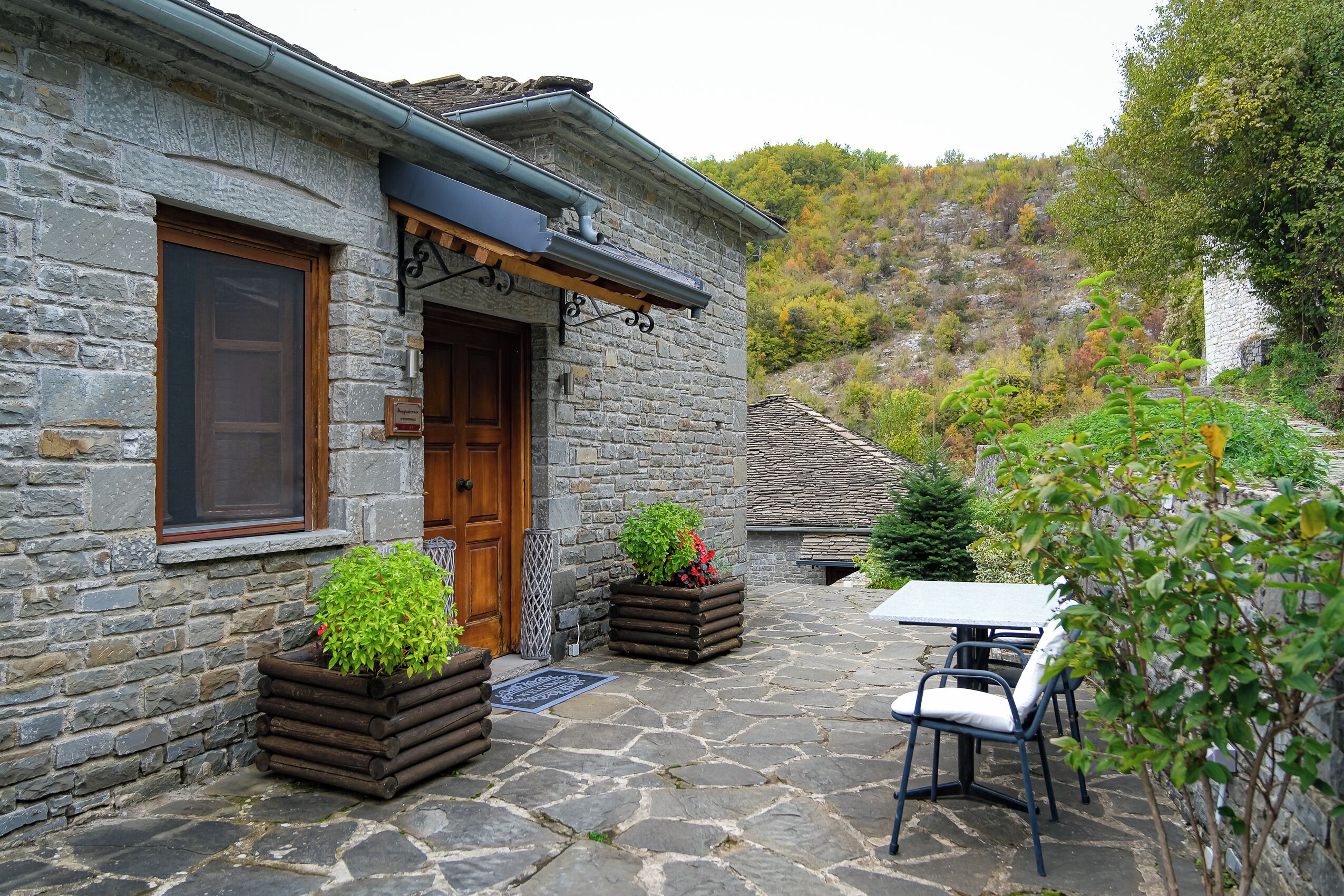 A stone building with a wooden door, outdoor seating, and planters with greenery.