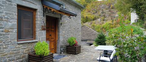A stone building with a wooden door, outdoor seating, and planters with greenery.