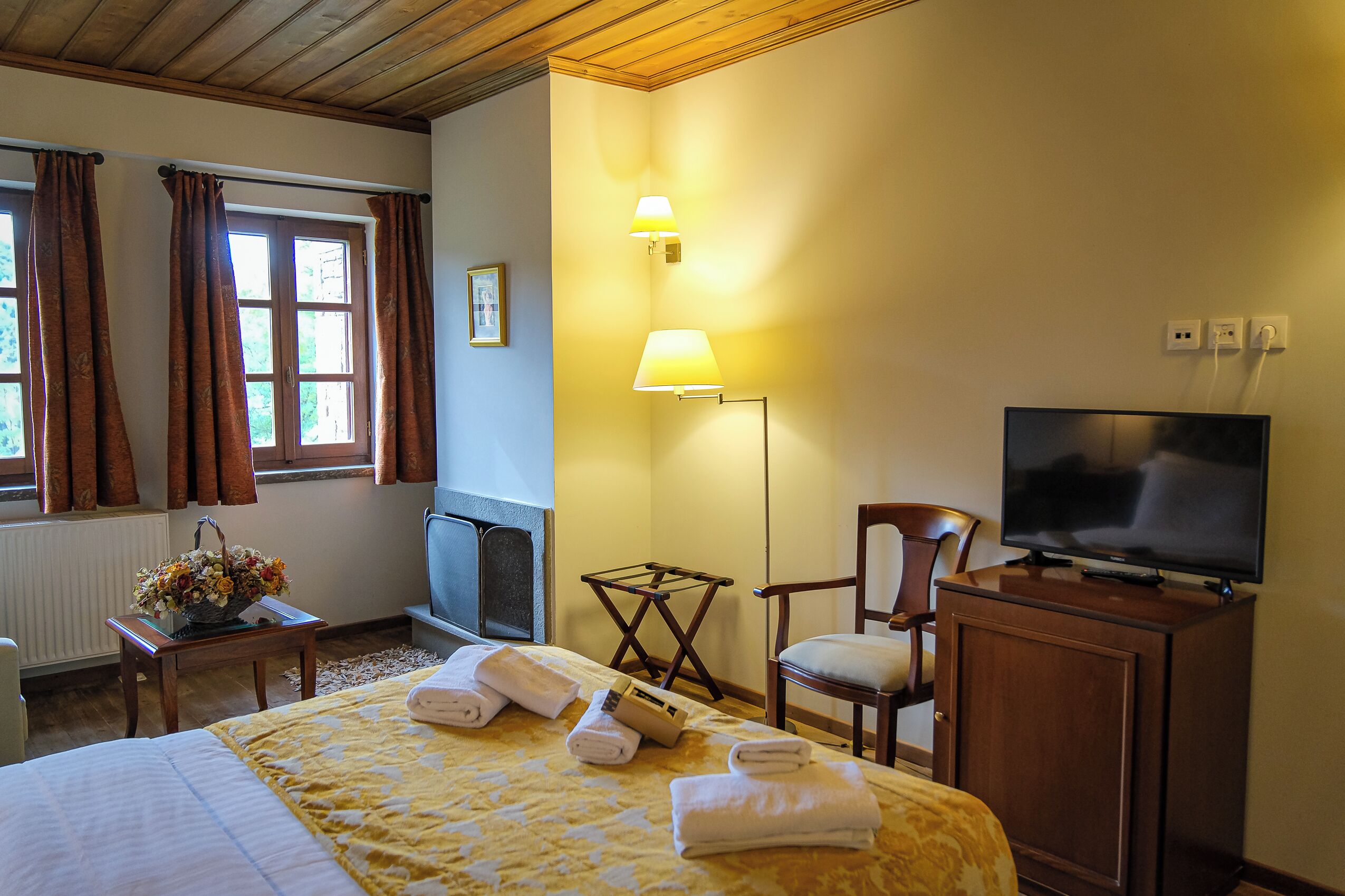 Ett hotellrum med en säng, en tv, en stol, en lampa och ett fönster med gardiner.