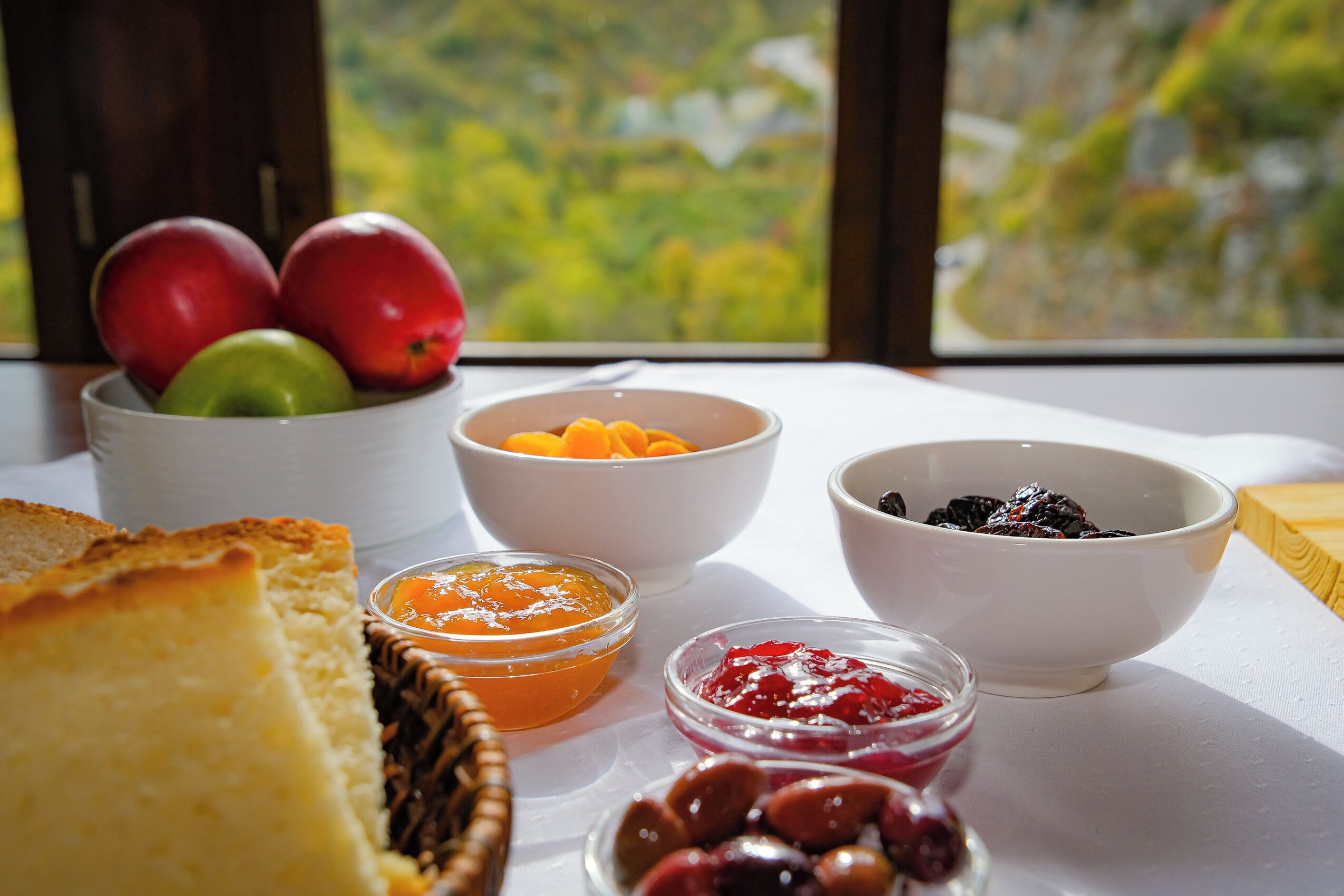 A table with various food items including bread, apples, and bowls of fruit preserves.
