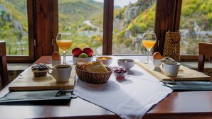 Una mesa de desayuno con muffins, café, jugo de naranja y tazones de fruta, con vistas a una montaña pintoresca.