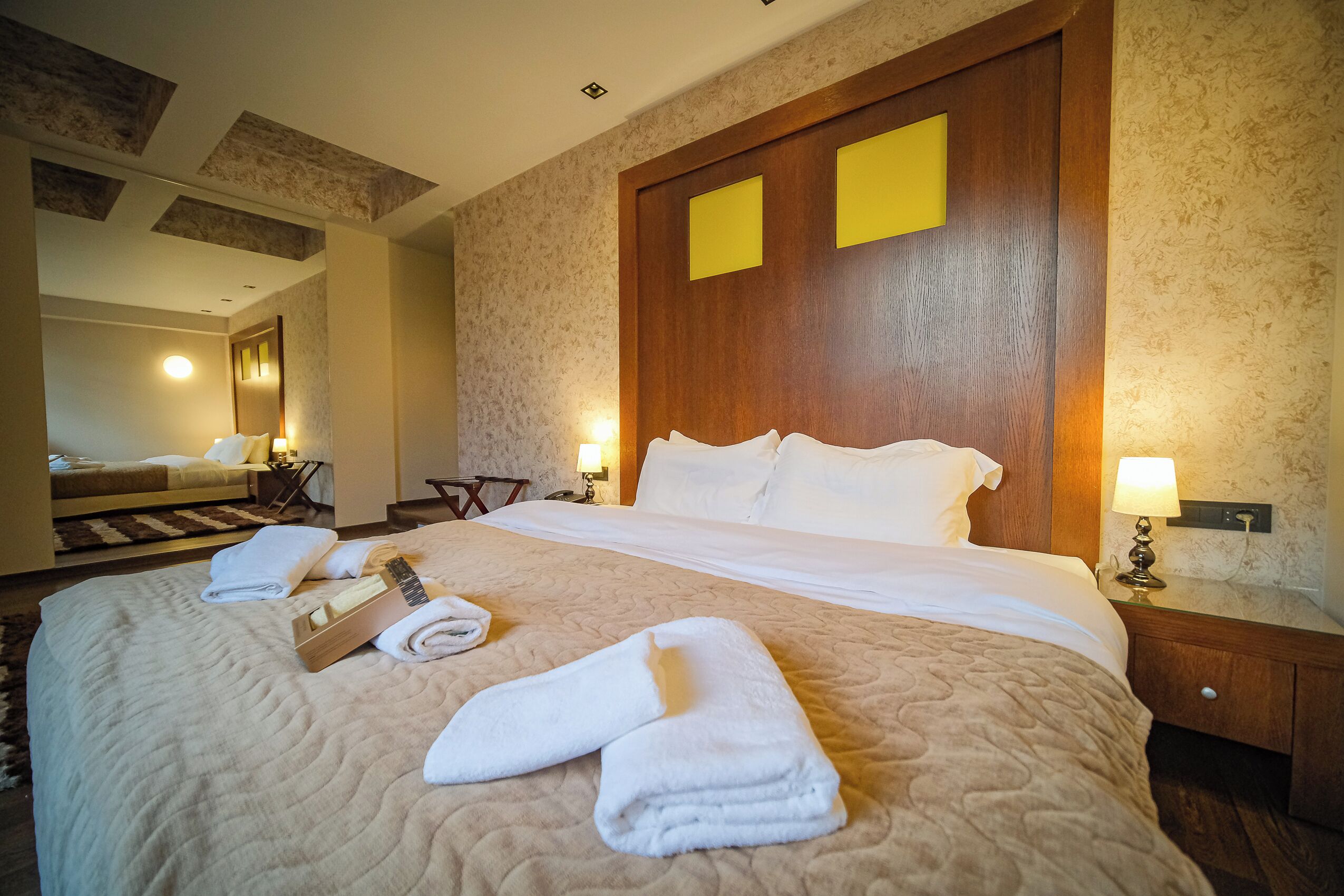 Ein Hotelzimmer mit einem großen Bett, zwei Nachttischlampen, einem Holzkopfstück und einem Spiegel an der Wand.