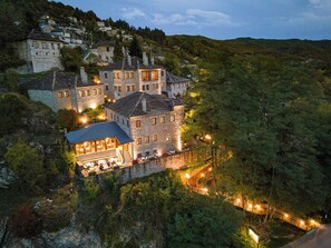 A stone building with multiple windows and a balcony, surrounded by lush greenery and a hillside. - Kipi Mountain Resort (Zagori)