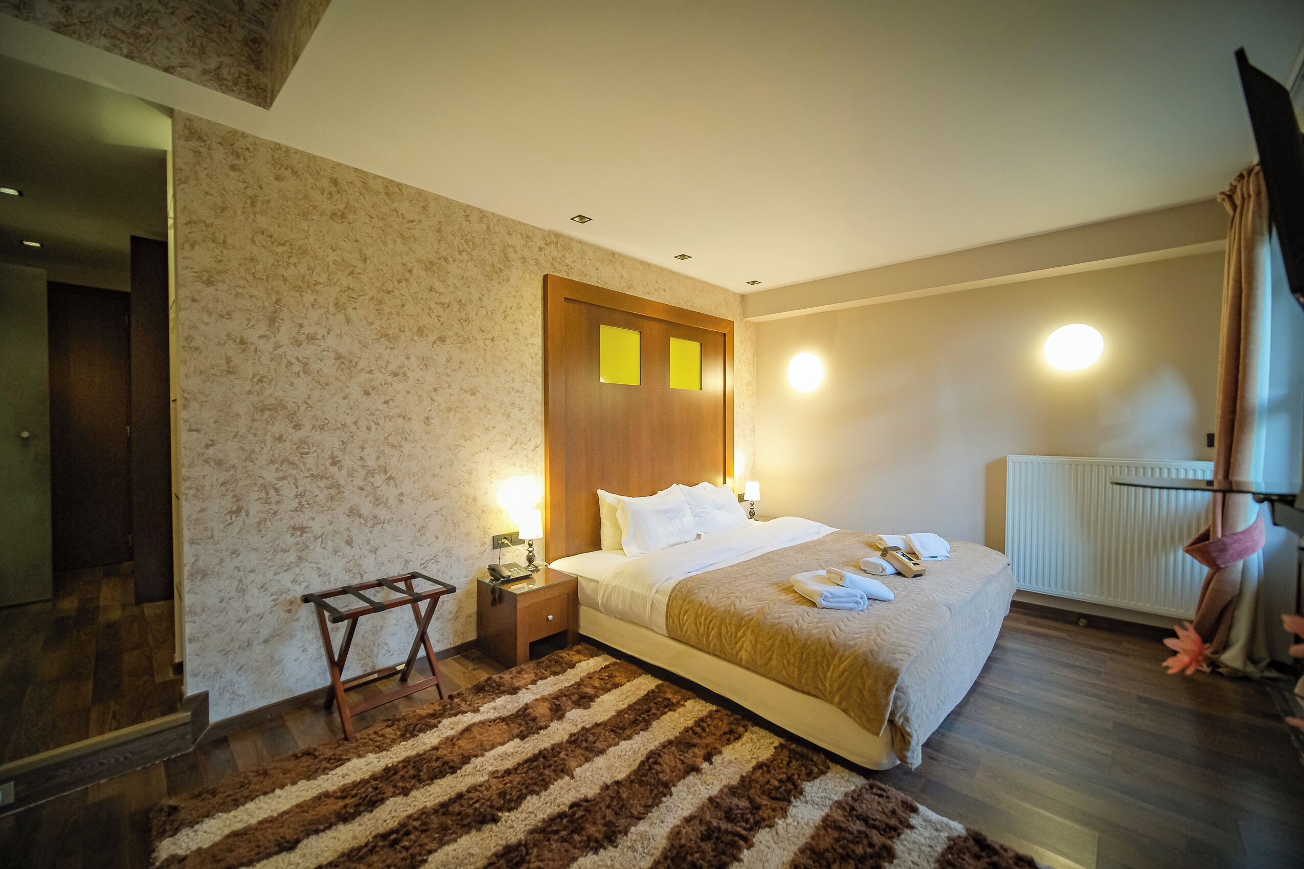 A hotel room with a large bed, a wooden headboard, a nightstand, a lamp, and a radiator.