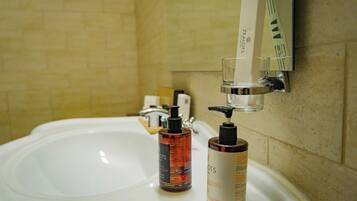 A bathroom sink with two bottles of Zealots products, a soap dispenser, and a glass of water.