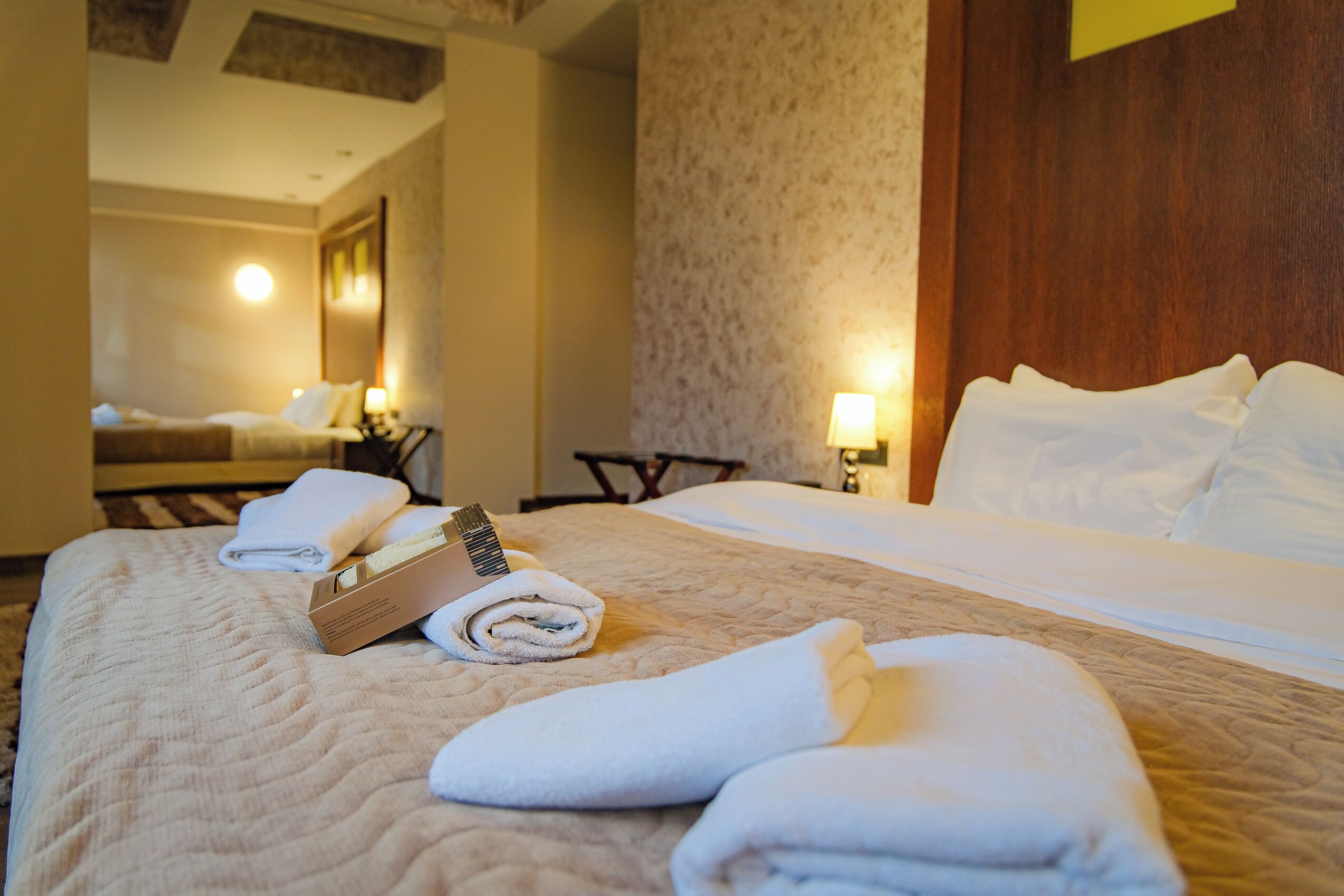 A hotel room with a neatly made bed, a bedside table with a lamp, and a wall-mounted mirror.