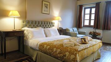 A neatly made bed with a floral bedspread, two bedside lamps, a bedside table with a phone, and a window with curtains.