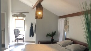 Quarto com cama de madeira, luminária pendente, planta em vaso e uma cadeira no canto.