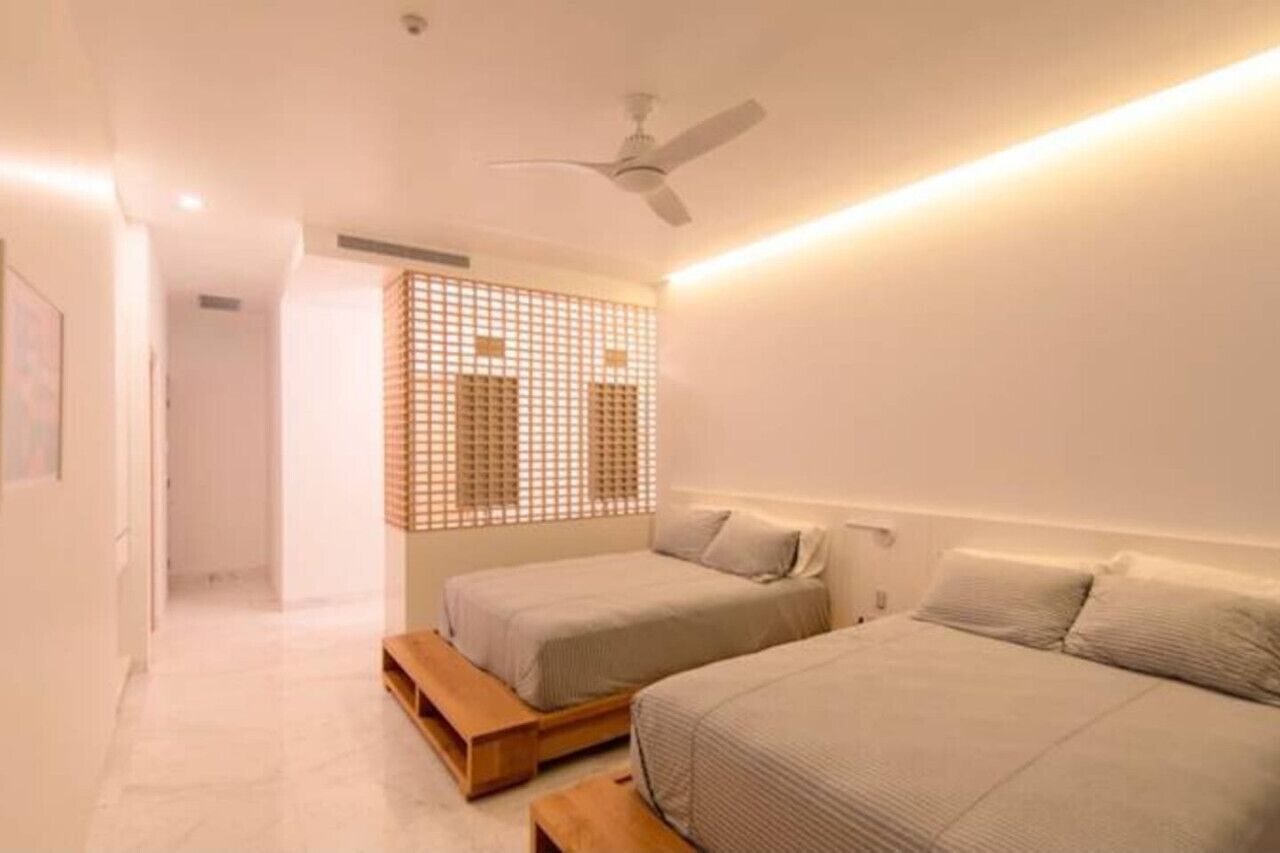 A bedroom with two beds, a ceiling fan, and a wall-mounted light fixture.
